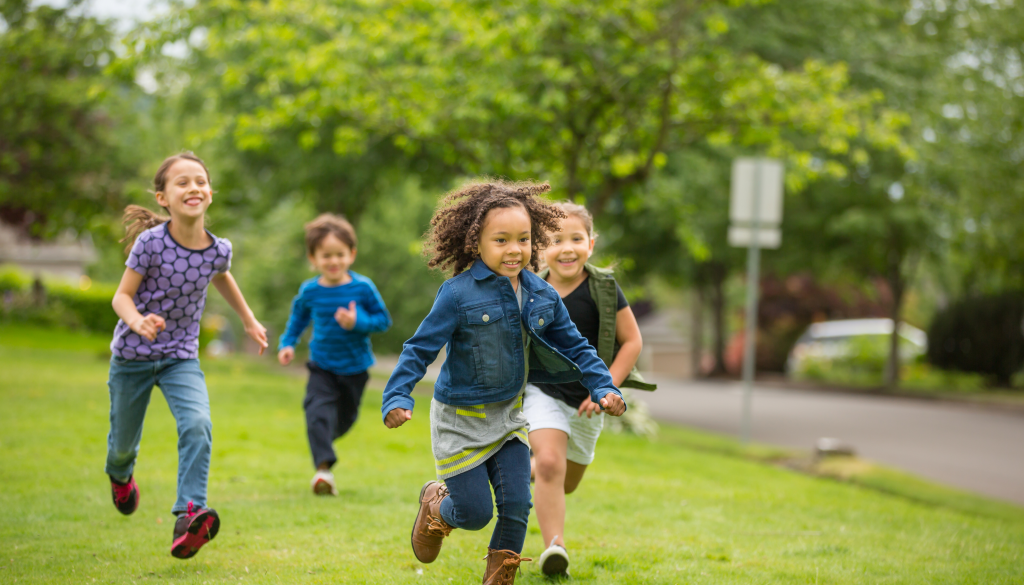 A vibrant, energetic scene of children actively engaged in physical play, showcasing the positive impact on their health. In the foreground, a group of young kids run, jump, and tumble on a grassy field, their faces filled with joy and excitement. The middle ground features a diverse array of motion-based activities, such as hopscotch, hula hoops, and ball games, all encouraging physical development and coordination. The background depicts a lush, verdant landscape with trees and a clear blue sky, creating a sense of natural, wholesome environment. The lighting is warm and soft, capturing the energy and vitality of the scene. The overall composition conveys the holistic benefits of active play on the physical, mental, and social well-being of children. دراسة علمية: اللعب الحركي وفوائده الصحية للأطفال
